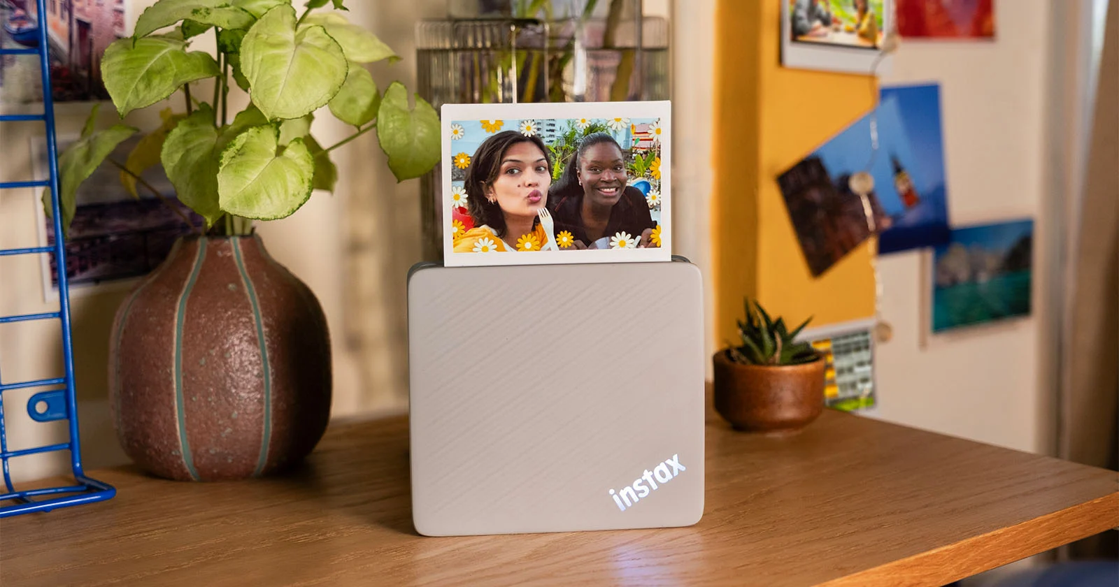 Принтер Instax Link Wide 2 на письменном столе печатает селфи двух девушек