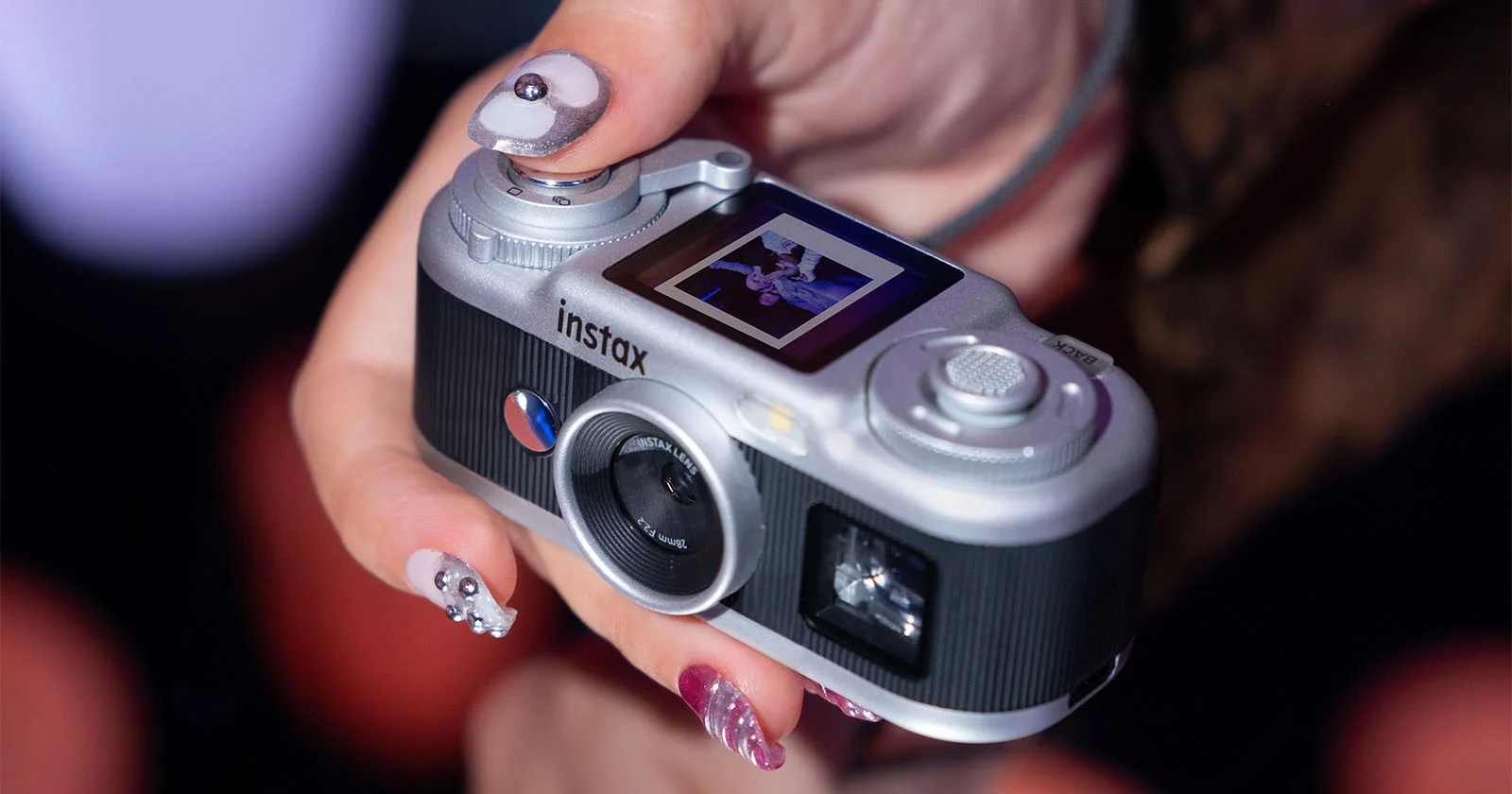 Instax Pal 2 в руке крупным планом: сверху виден небольшой экран с фотографией и кнопка спуска