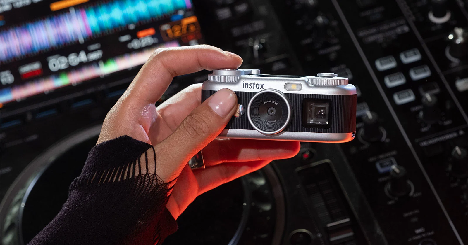 Камера Instax Pal 2 в руке на фоне диджейского пульта с подсветкой