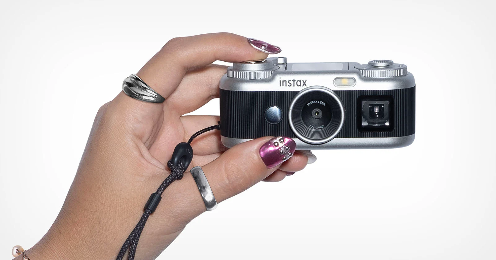 Серебристо-чёрная камера Fujifilm Instax Pal 2 в женской руке на белом фоне